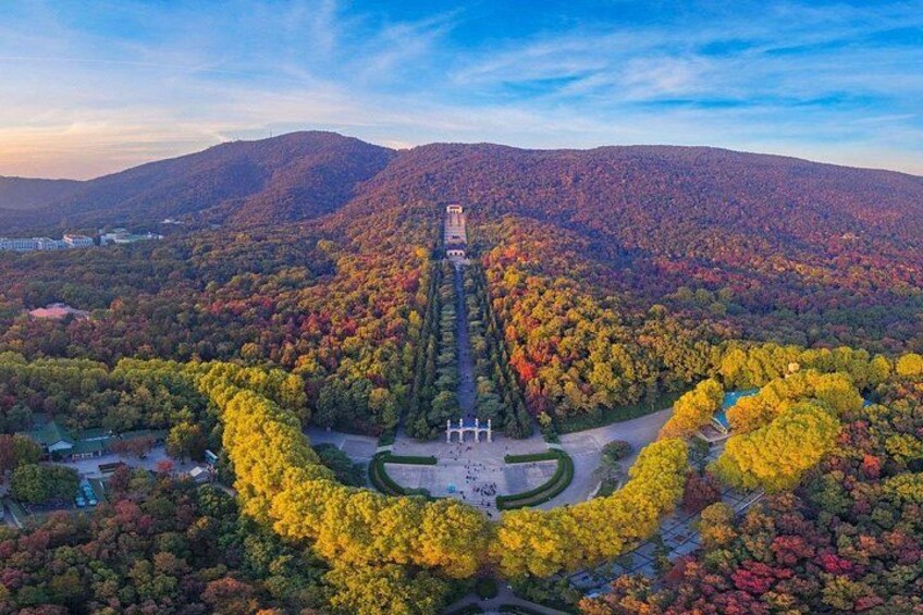 A landscaped garden with a central fountain, surrounded by trees in autumn colors, and a mountain in the background. 3