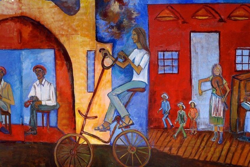 A mural with a person on a bicycle, a woman playing a violin, and children in a red building. 2