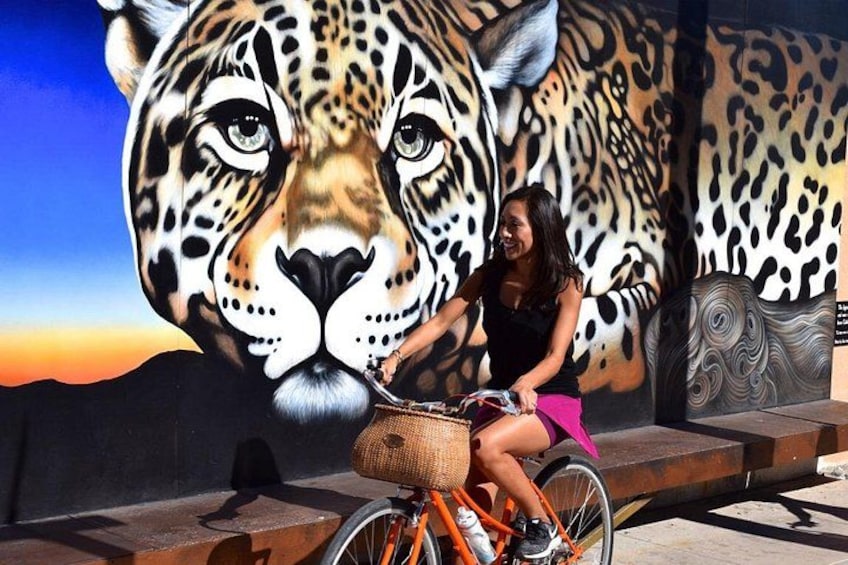 A person on a bicycle with a large mural of a leopard in the background. 4