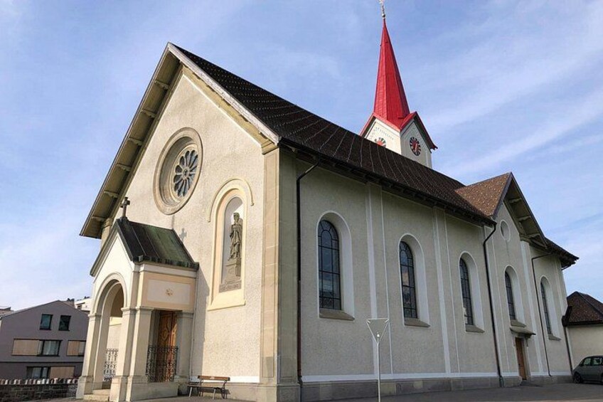 A church with a red spire, a clock, and a statue on the facade. 3
