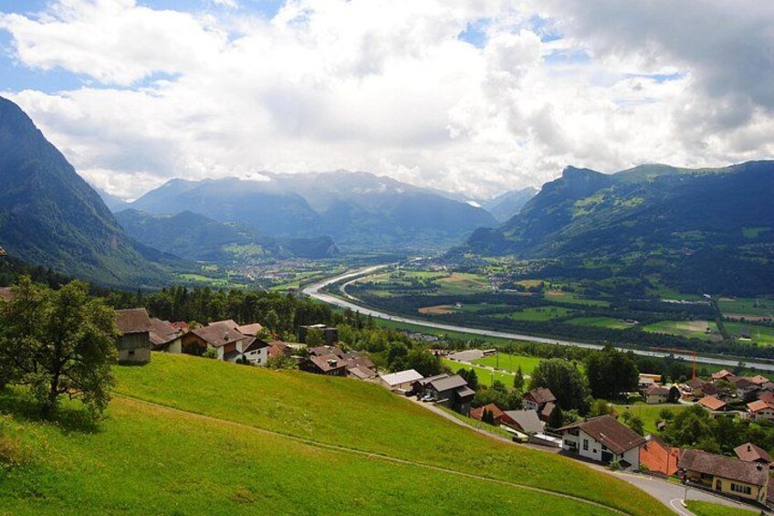 A valley with a river, houses, and mountains. 5