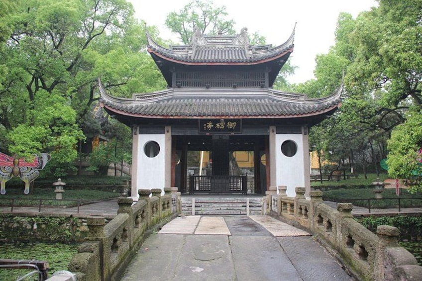 A traditional Chinese gate with intricate roof design, surrounded by lush greenery and a stone pathway leading through it. 1