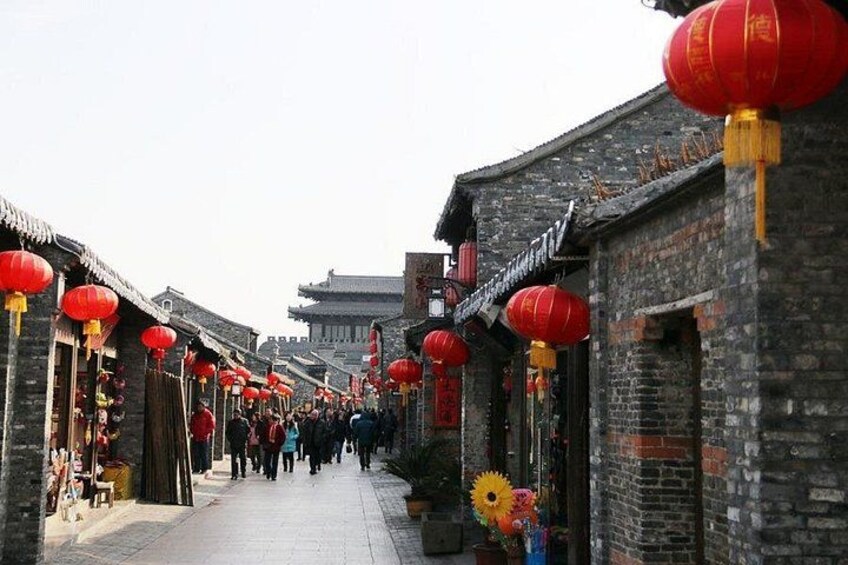 A traditional street with red lanterns, brick buildings, and a crowd of people. 2