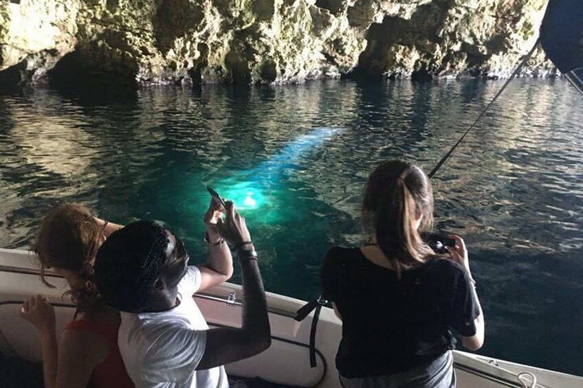 Tres personas en un bote pescando en aguas azules y cristalinas, con acantilados rocosos al fondo. 2
