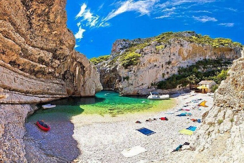 A coastal beach with clear turquoise water, rocky cliffs, and a small boat anchored near the shore. 2