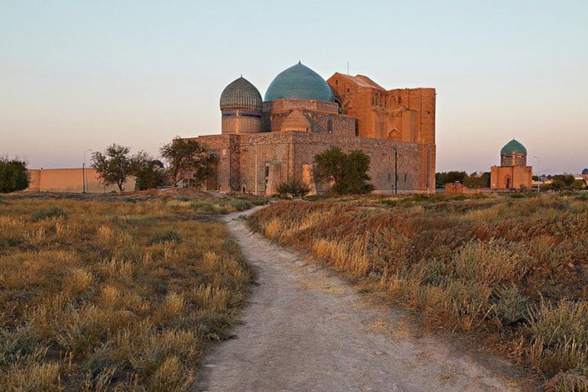 Ein historisches Gebäude mit Kuppeldächern, ein Feld aus trockenem Gras und ein Weg dorthin. 1