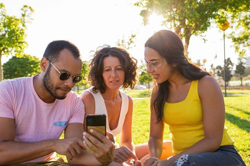 Three people sitting on a bench outdoors, looking at a smartphone. 2
