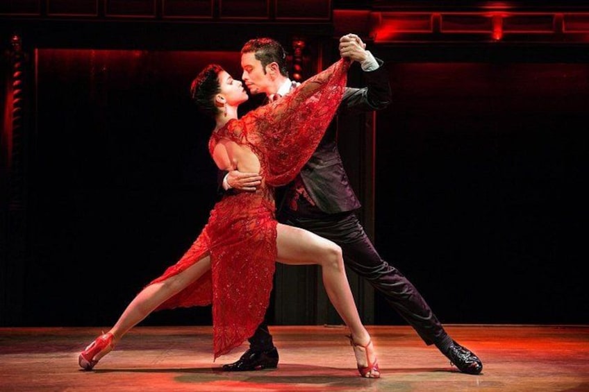 Un couple danse sur une scène, avec un fond sombre et un éclairage rouge. 1