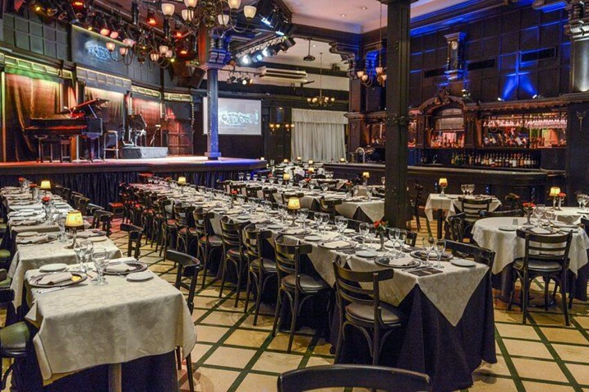 Une salle de banquet avec des tables dressées pour un événement formel, une scène avec des instruments de musique et un espace bar. 3