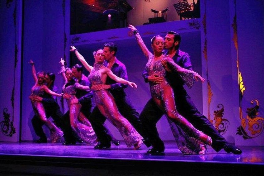 En dansföreställning med dansare i glittrande kostymer på en scen med en lila bakgrund. 4