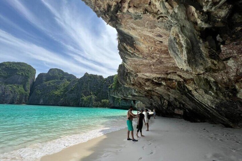 Ein Strand mit klarem türkisblauem Wasser, Menschen, die am Sand stehen, und eine große Felsformation. 2