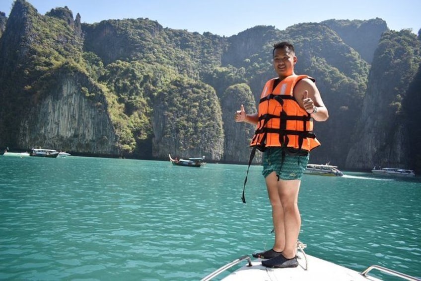 Eine Person in einer Rettungsweste auf einem Boot, umgeben von klarem, blauem Wasser und felsigen Klippen. 2