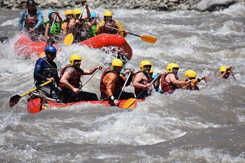 Een groep mensen in een rode raft die een rivier met witte watervallen trotseert. 4