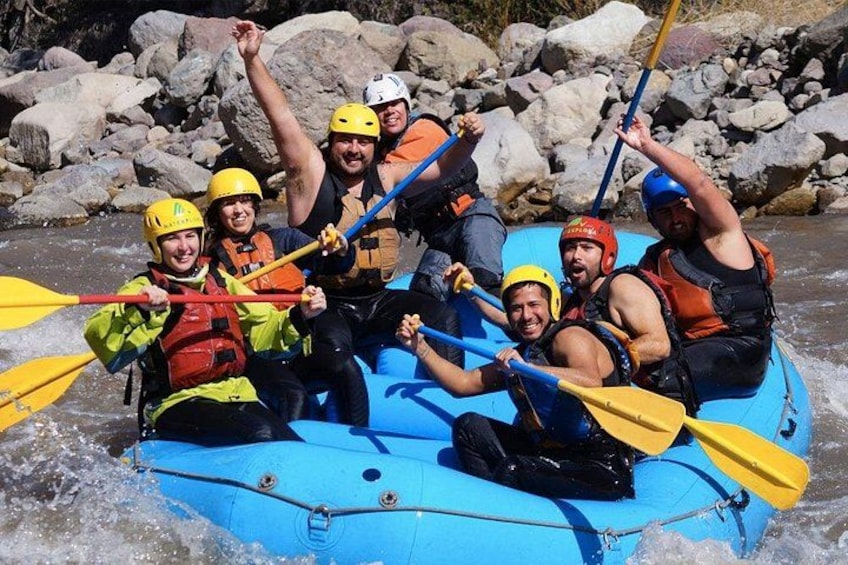Een groep mensen in een blauwe vlot op een rivier, met rotsen op de achtergrond. 1