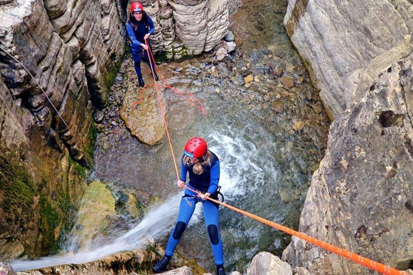 Two people rappelling down a rocky cliff with a rope. 1