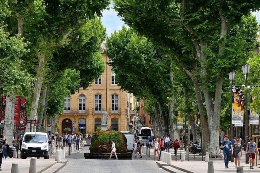Une rue bordée d’arbres, avec des piétons, un bâtiment historique et des voitures garées. 2