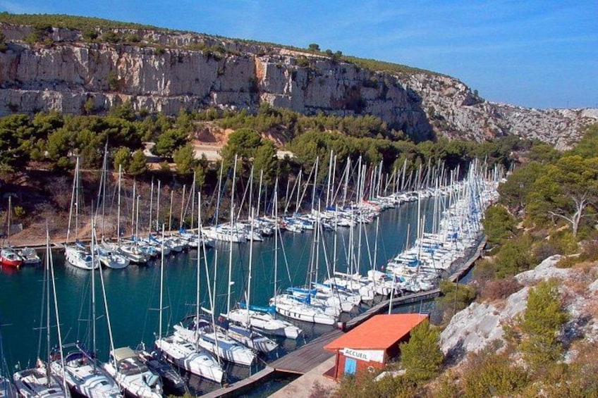 Un port de plaisance où de nombreux voiliers sont amarrés le long d’un étroit canal, entouré de falaises rocheuses et d’une végétation clairsemée. 5