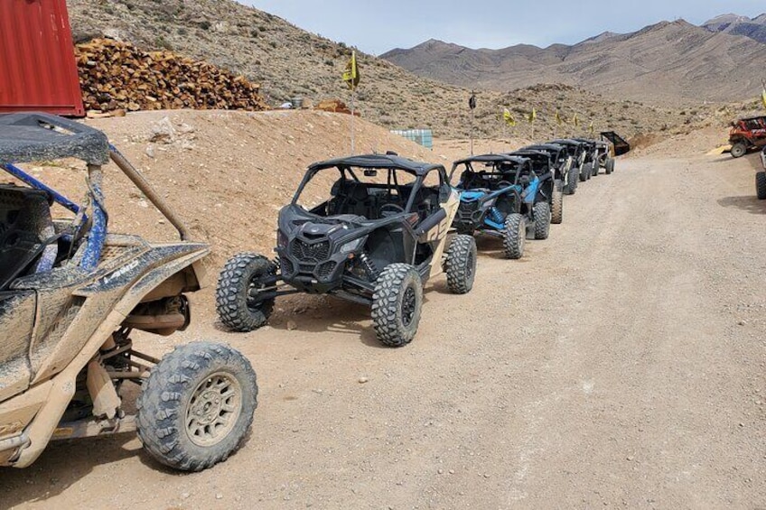 A row of off-road vehicles parked on a dirt road in a mountainous area. 2