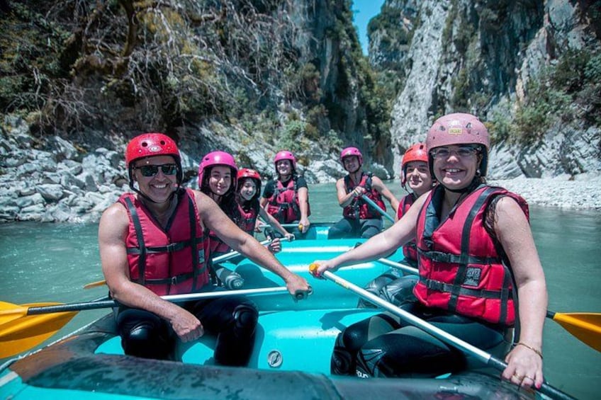 A group of people in a blue raft on a river, wearing red helmets and life jackets. 2