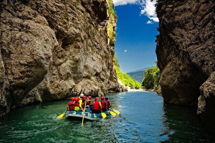 A group of people in a raft navigating through a narrow water channel between rocky cliffs. 1