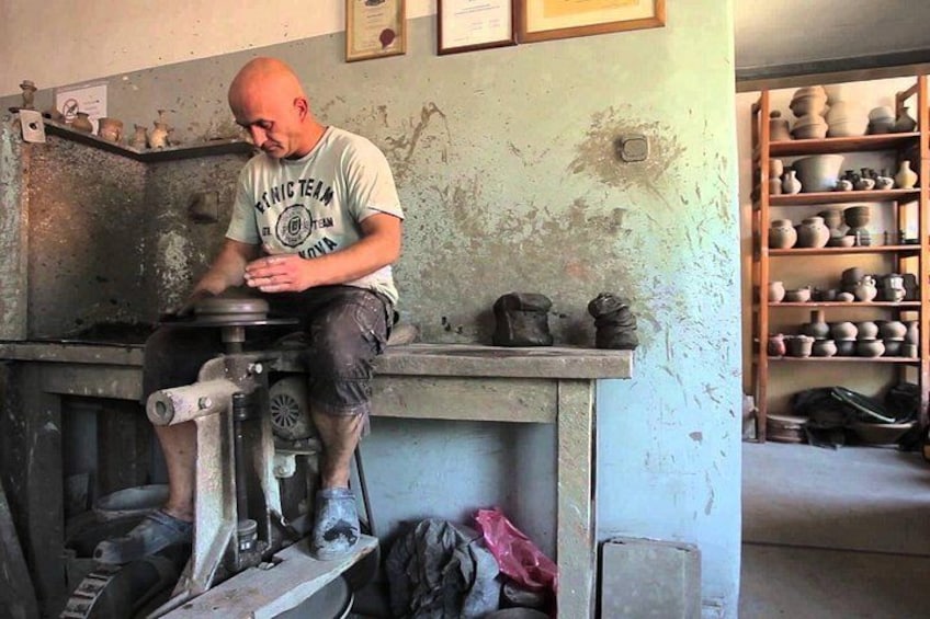 Una persona trabajando cerámica en un torno alfarero en un taller, con estantes llenos de piezas de cerámica al fondo. 5