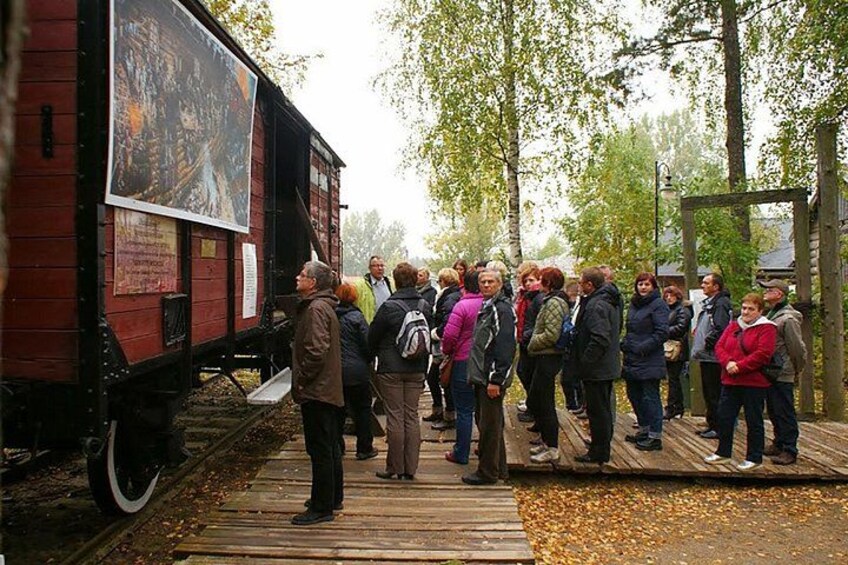 Un grupo de personas de pie sobre una plataforma de madera junto a un vagón de tren rojo con un cartel grande. 2