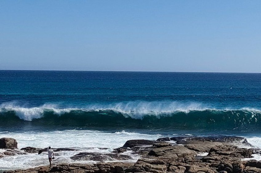 A rocky shoreline with waves crashing onto the rocks under a clear blue sky. 2
