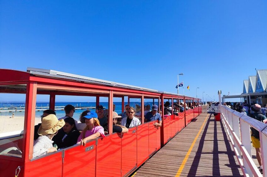 A red tram on a pier with people seated inside, overlooking the beach. 1