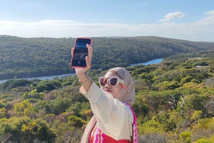 A person taking a photo with a smartphone, surrounded by a lush landscape with trees and a lake in the background. 3