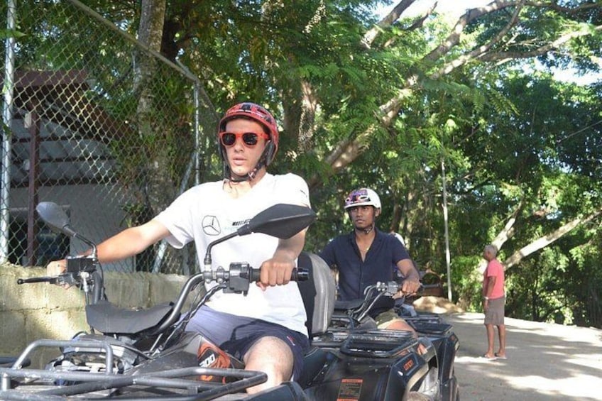 Two people on ATVs, one wearing a helmet, and a fence in the background. 5