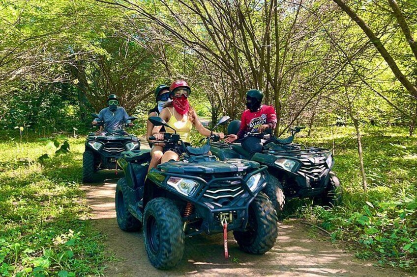 Four people on ATVs on a dirt path surrounded by greenery. 1
