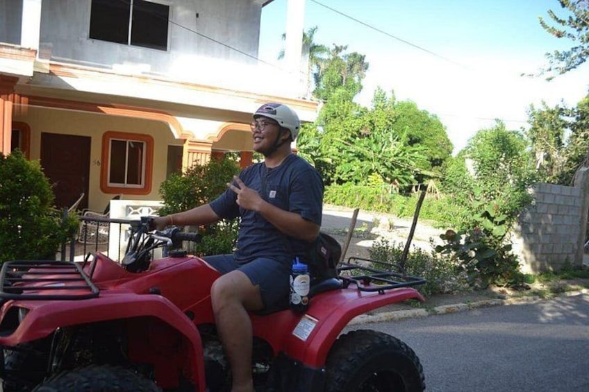 A person riding a red ATV on a street with houses and greenery in the background. 2