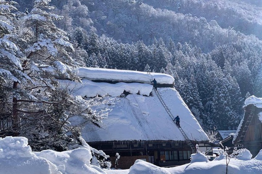 A snow-covered house with people shoveling snow from the roof. 3