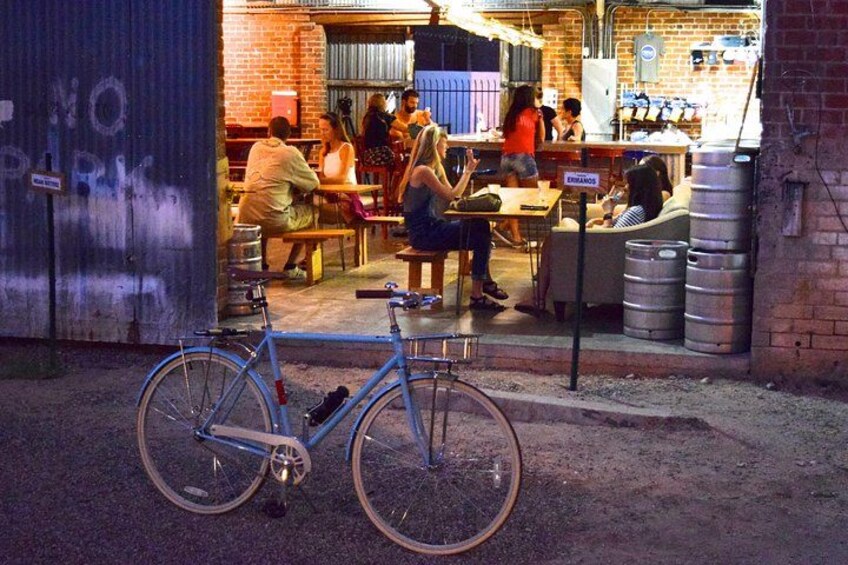 En cykel parkeret foran en bygning, hvor folk sidder ved borde indeni. 1