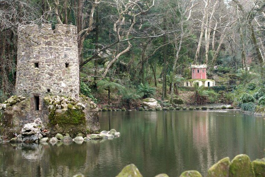 A stone tower, a small red building, and a calm lake surrounded by trees. 3