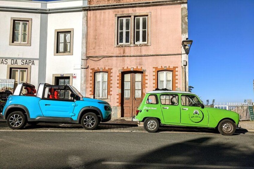 Two vintage cars parked on a street, a blue convertible and a green car with a logo. 5