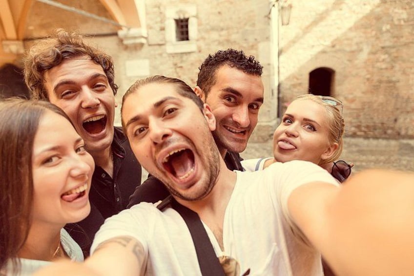 Un groupe de personnes prenant un selfie dans un cadre extérieur, avec des bâtiments en pierre en arrière-plan. 3