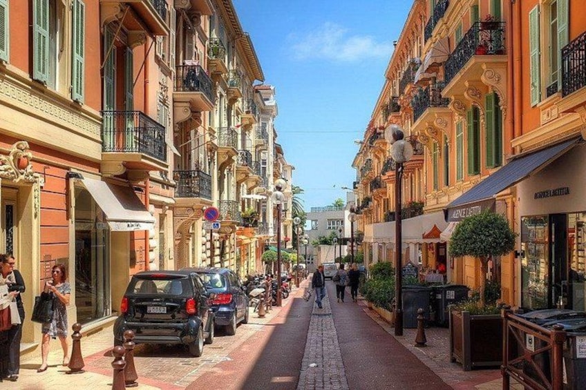 A street lined with colorful buildings, parked cars, and pedestrians. 4