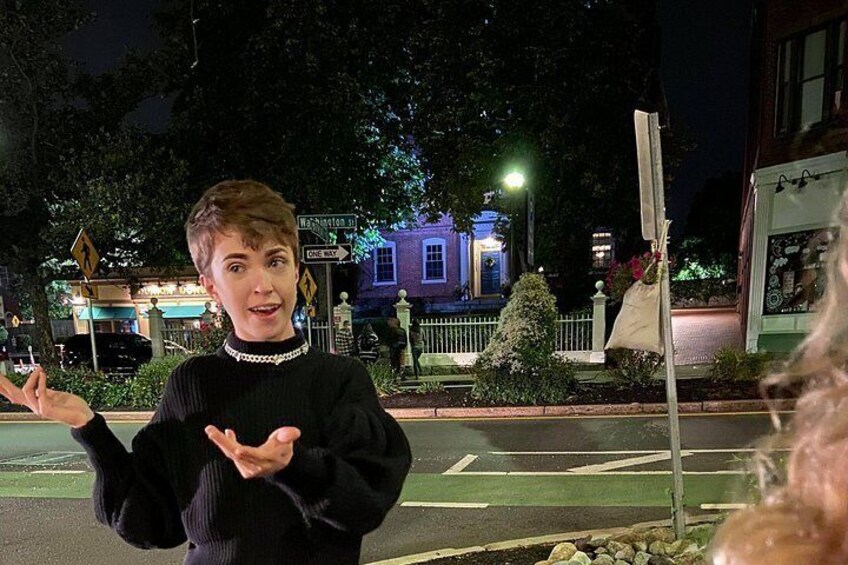 A person gesturing with hands, a street with a crosswalk, and a building with illuminated windows in the background. 3