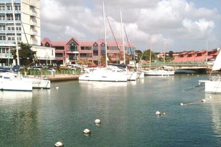 A marina with several sailboats docked, a building with a red roof, and a bridge in the background. 1