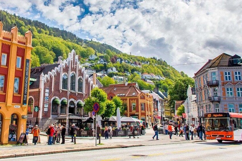 A bustling street with historic buildings, a tram, and a mountainous backdrop. 3