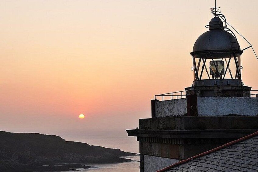 A lighthouse at sunset with the sun near the horizon, a rocky coastline, and a clear sky. 2