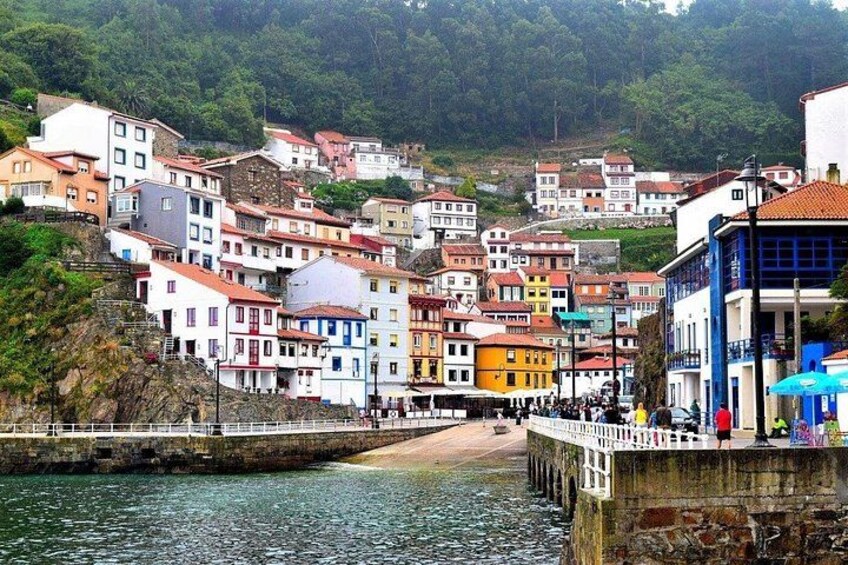 A coastal town with colorful buildings, a pier, and a hillside in the background. 1