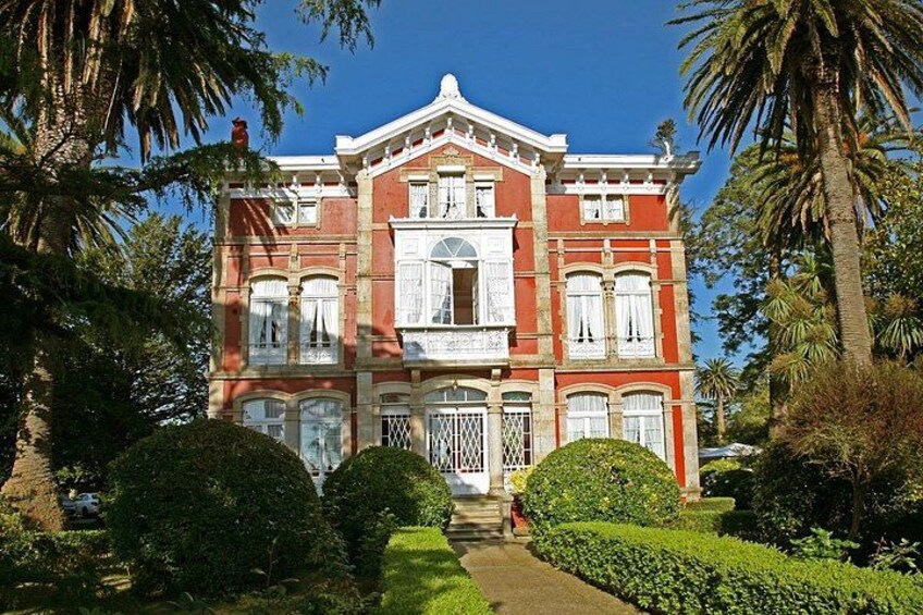 A large, red brick building with white trim and multiple windows, surrounded by well-manicured gardens and palm trees. 4