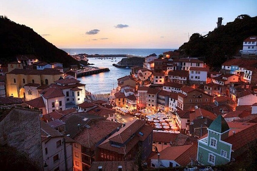 A coastal town at dusk with buildings, a harbor, and a hill in the background. 3