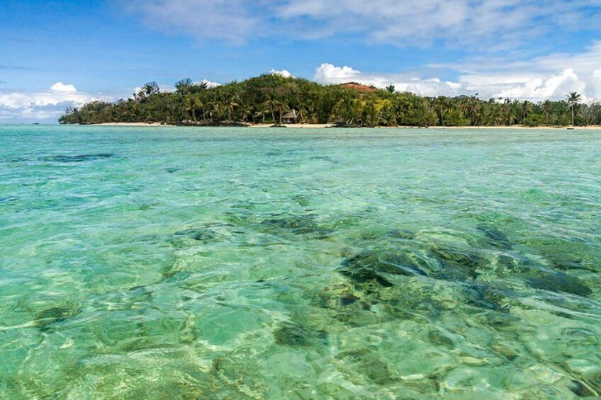 A tropical beach with clear turquoise water, a sandy shore, and a forested island in the background. 2