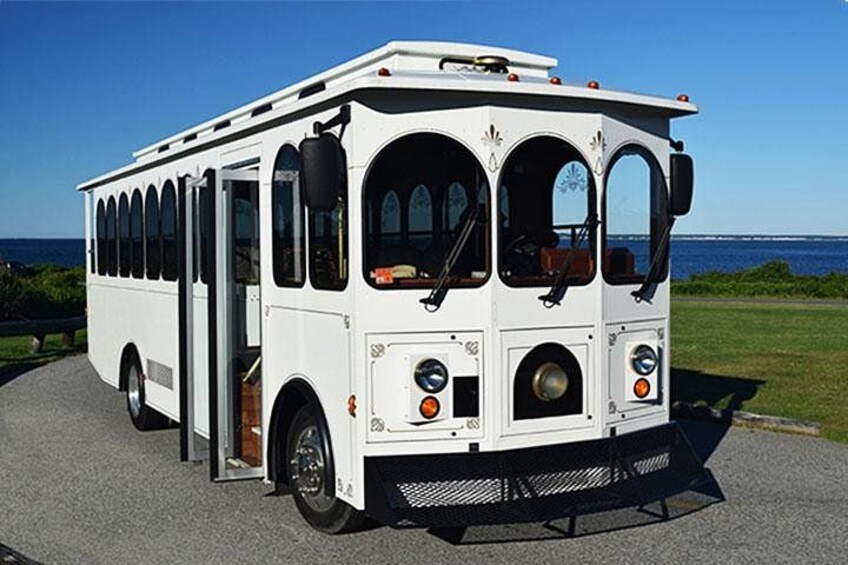 A white bus with a front open door, parked on a paved surface with a grassy area and a body of water in the background. 1