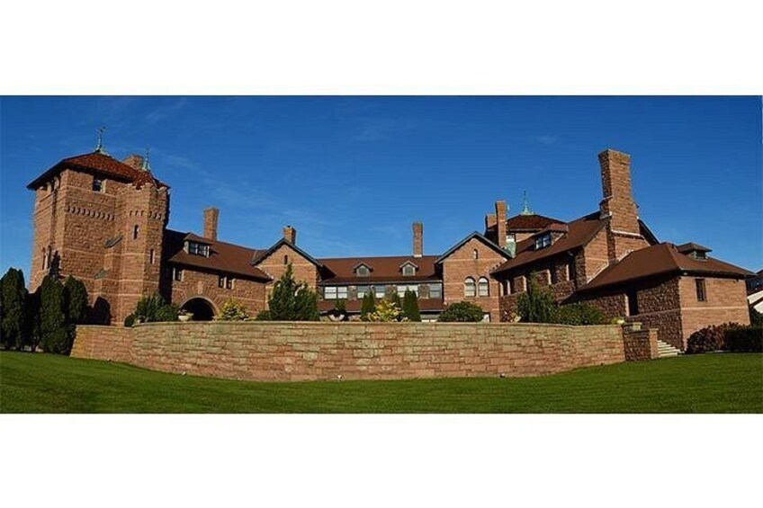 A large brick building with a tower, surrounded by a well-maintained lawn and a stone wall. 2