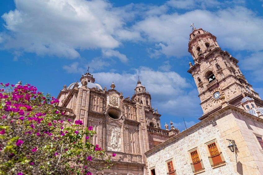 Una iglesia histórica con campanario y cúpulas, rodeada de flores rosadas. 4