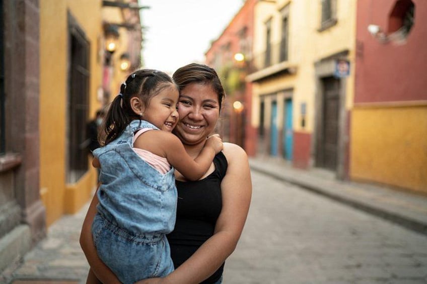 Una persona sostiene a un niño en una calle urbana con edificios coloridos. 3